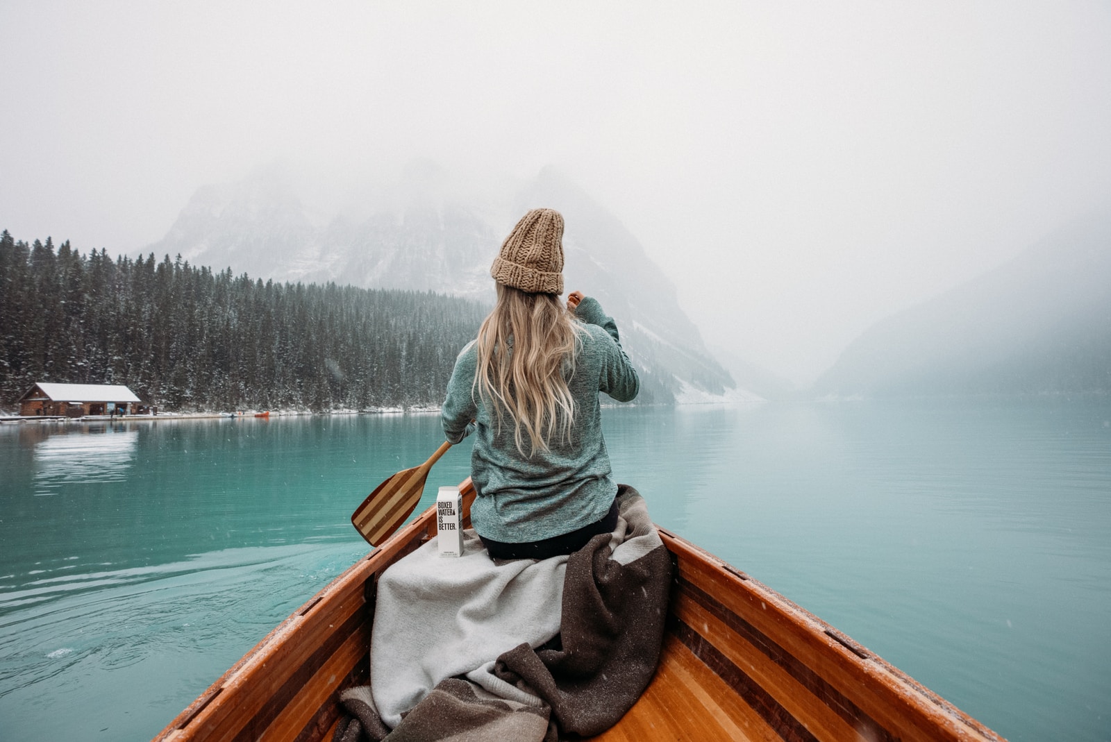 woman in gray hoodie sitting on brown wooden boat on lake during daytime