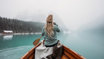 woman in gray hoodie sitting on brown wooden boat on lake during daytime